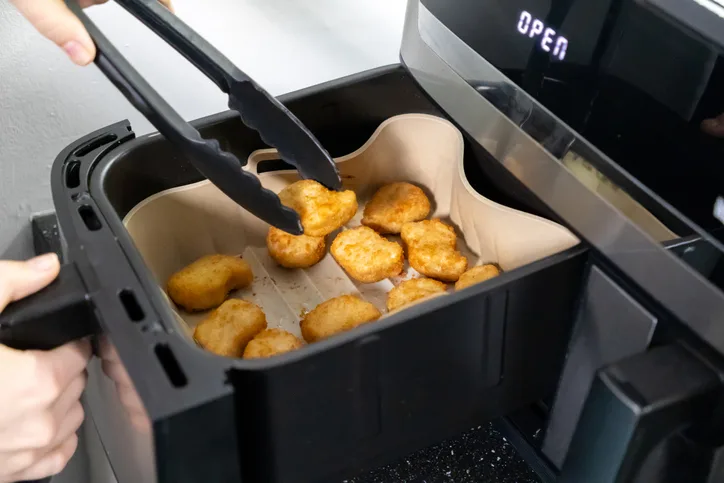 Dando la vuelta a los nuggets de pollo en la cesta de la freidora de aire