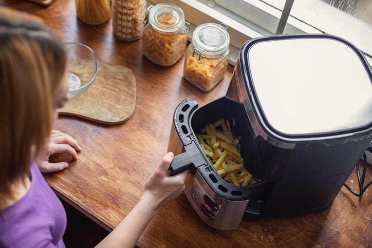 Persona sacando la cesta de una freidora de aire con patatas fritas
