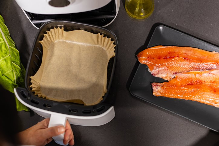 Lomos de salmón crudos junto a la cesta de la freidora de aire con papel